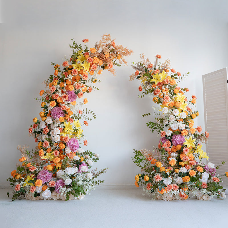 An elegantly designed artificial flower arch with a moon shape, featuring a vibrant color scheme with orange, pink, white, and yellow flowers.