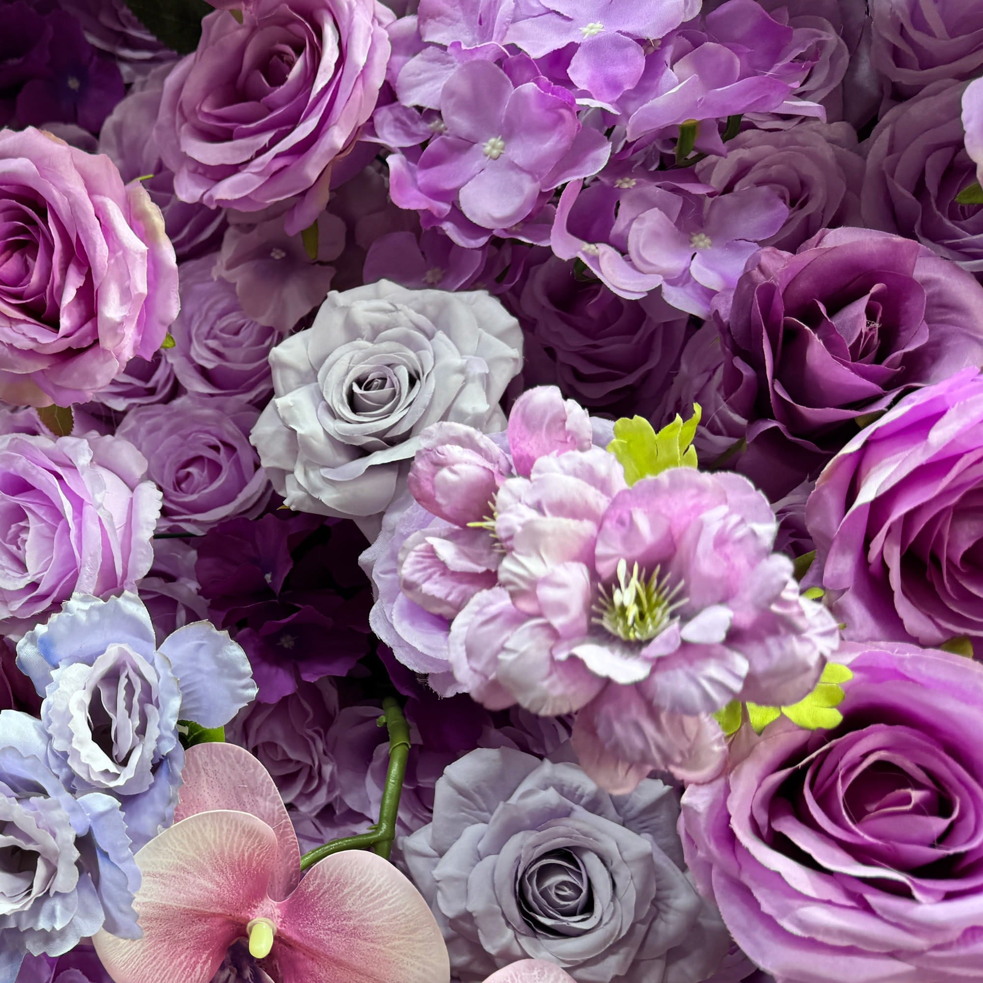This image showcases a rich arrangement of artificial flowers. Prominent are roses in various shades of purple, from light lavender to deep violet, along with some pink - hued orchids. There are also delicate white - tinged blooms and clusters of small white flowers. The color palette creates a harmonious blend of cool tones, exuding a romantic and elegant style, ideal for event decor.