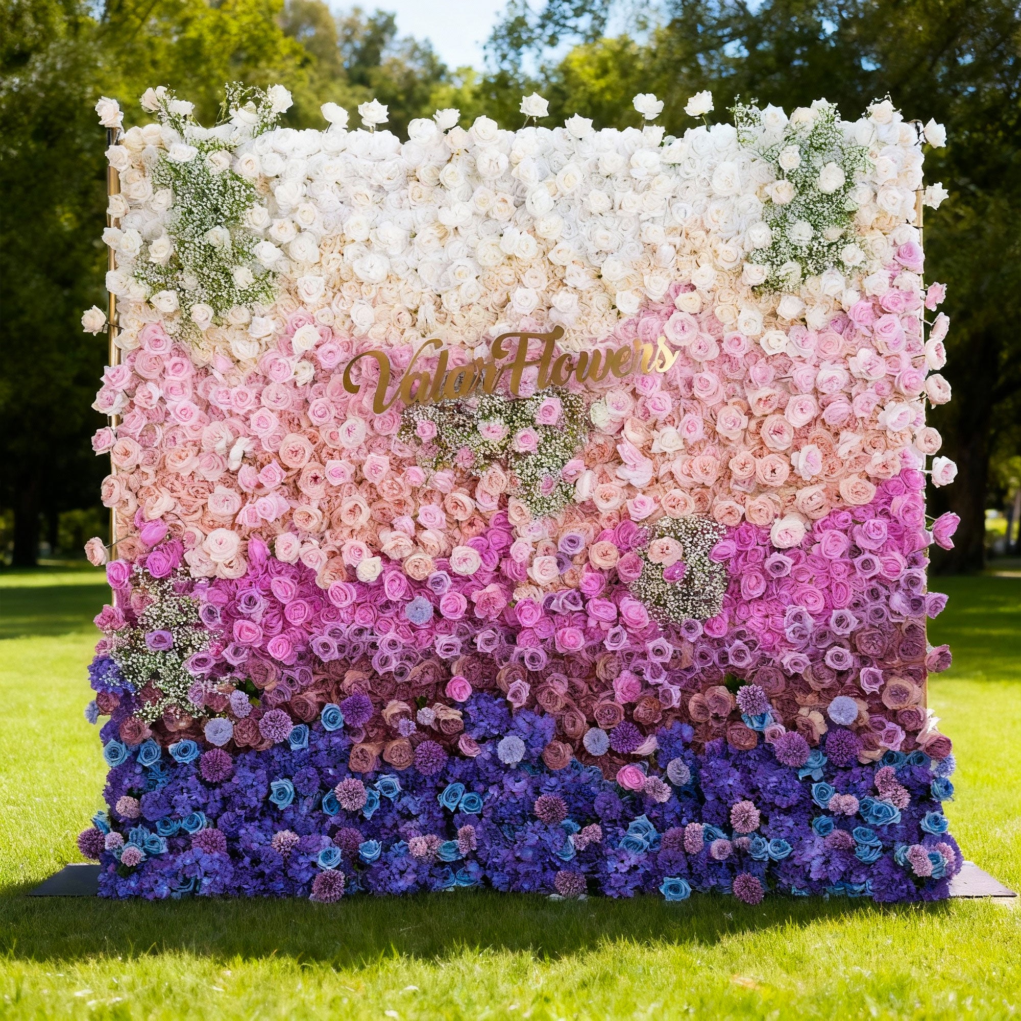 Floral wall with a gradient of colors and 'Vela Flowers' branding in an outdoor setting.