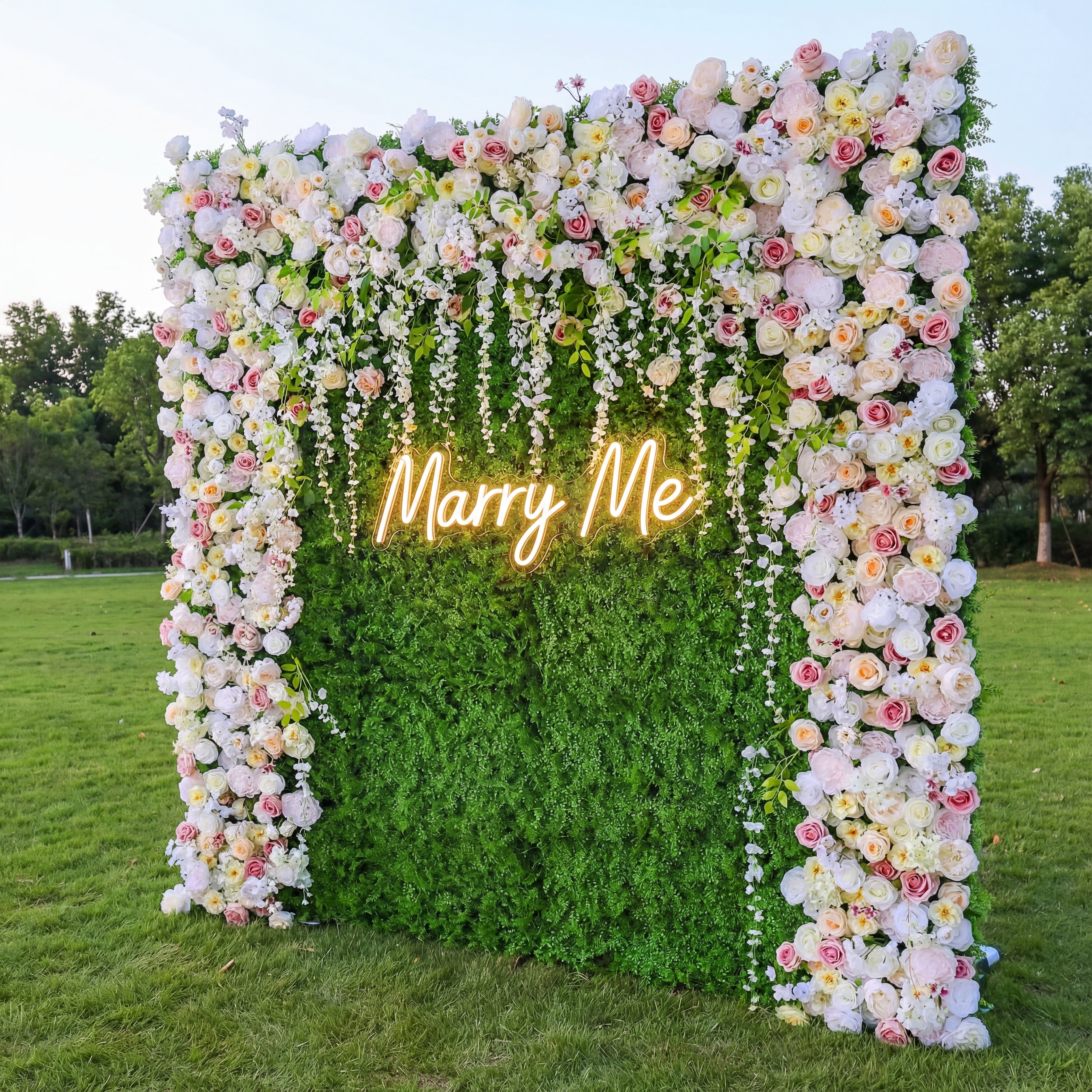 Floral arch with 'Marry Me' neon sign on a grassy field