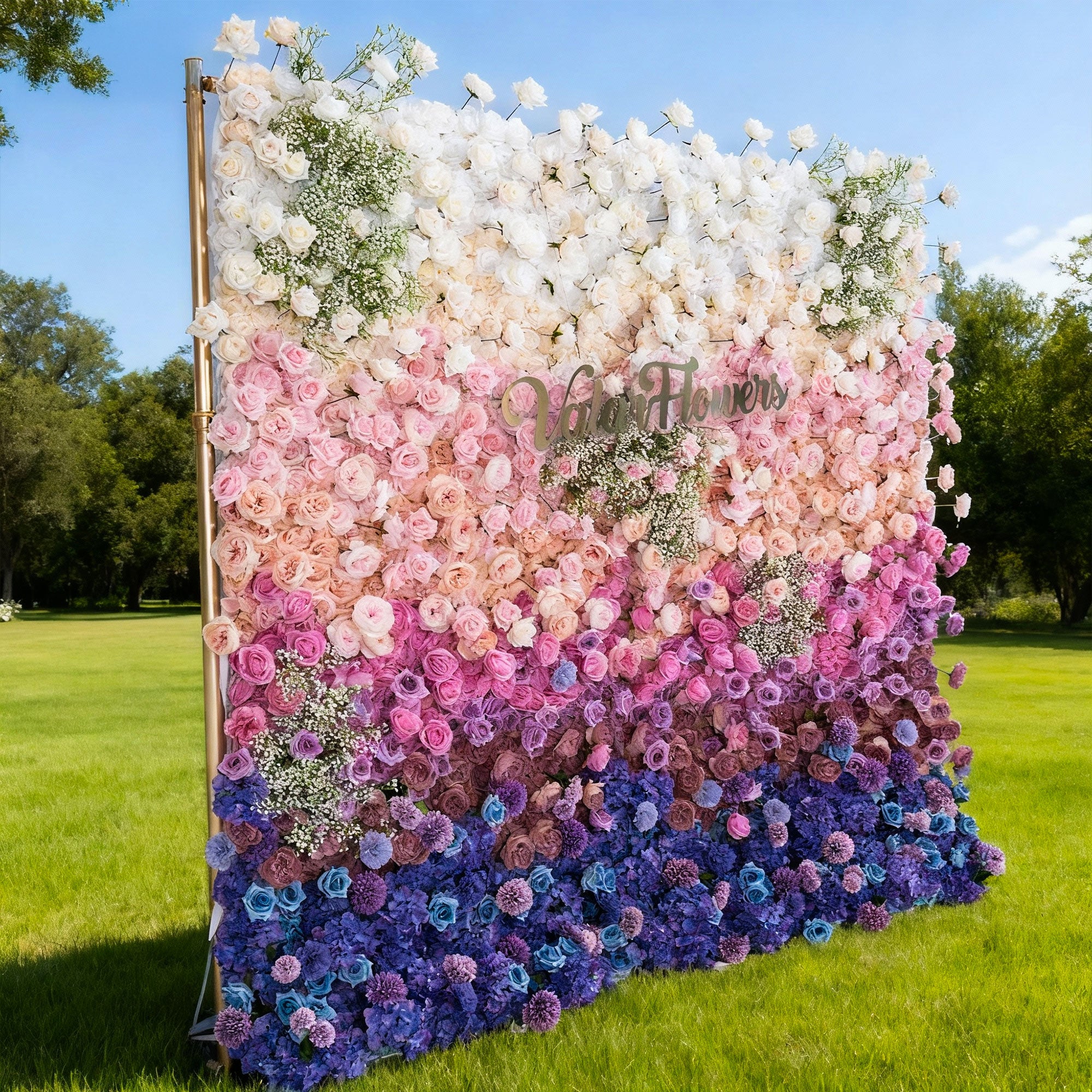 Floral wall with a gradient of white, pink, purple, and blue flowers in an outdoor setting.