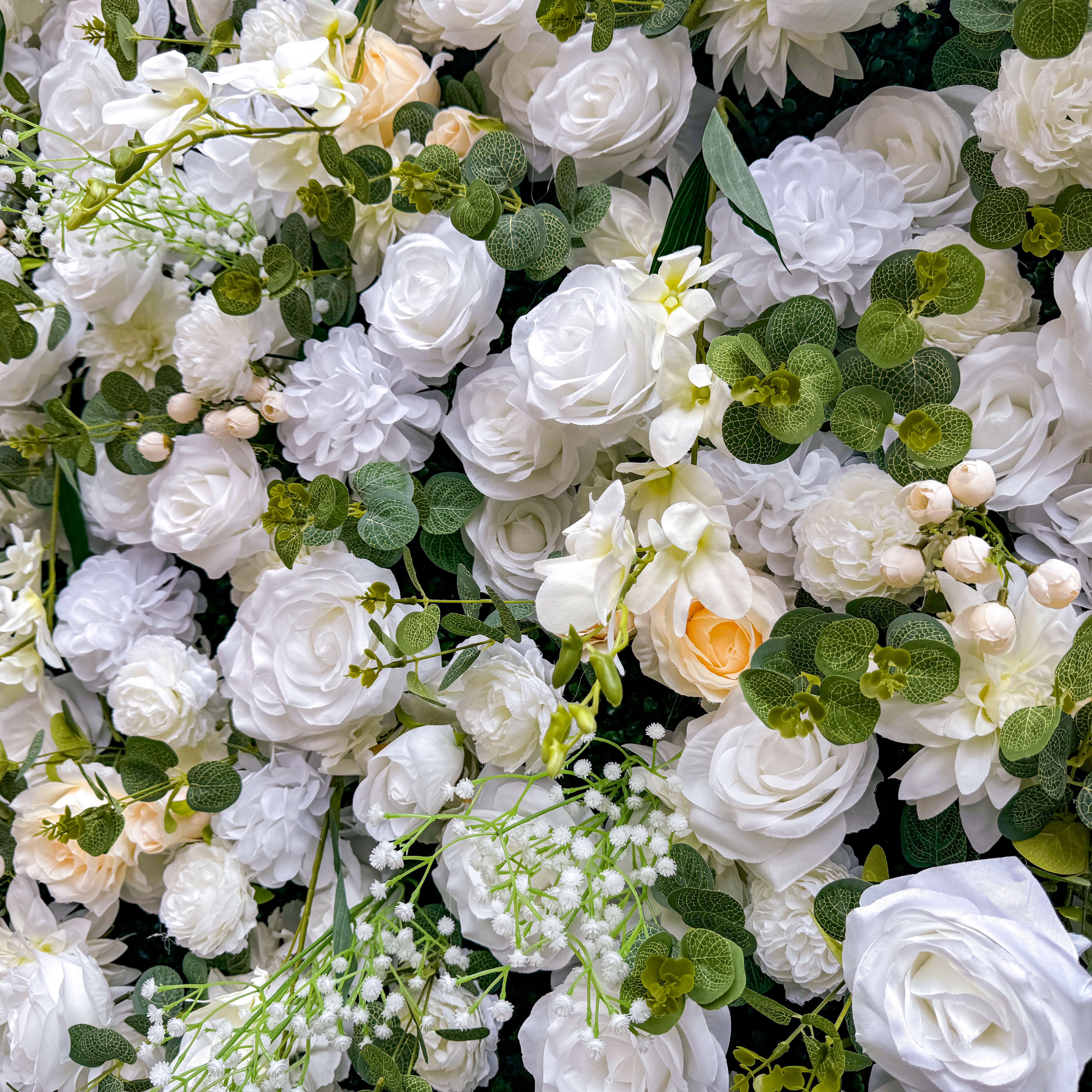 This artificial flower wall is a sight to behold. It is densely packed with a variety of white and cream - colored flowers, such as roses and lilies. The flowers are complemented by lush green leaves, creating a rich and elegant appearance. It is perfect for weddings or events, providing a romantic and beautiful backdrop.
