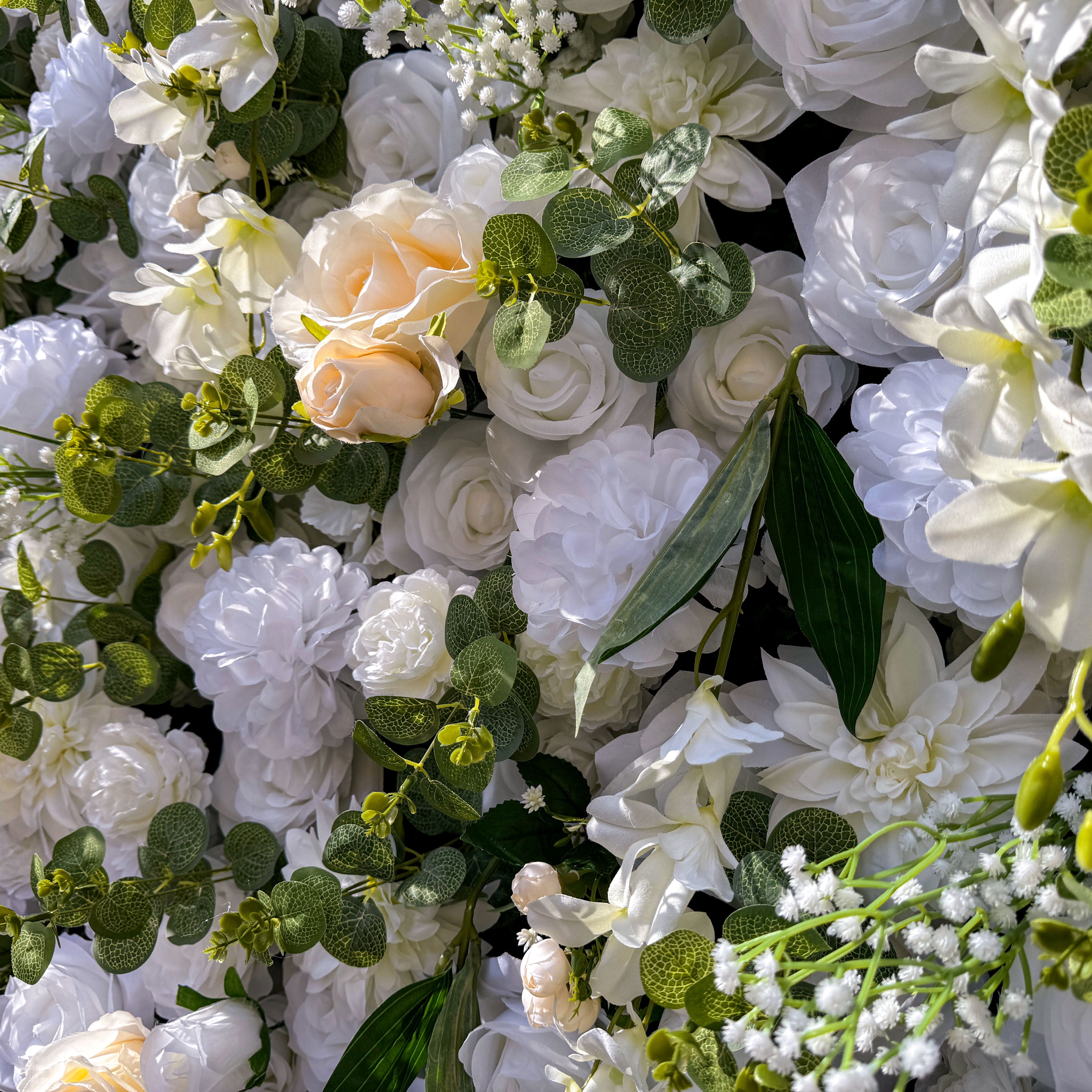 This artificial flower wall is a stunning piece. It is densely packed with a variety of white and off - white flowers, including roses and lilies. The flowers are complemented by lush green leaves and small floral buds, creating a rich and textured appearance. It's perfect for weddings or events, providing an elegant and romantic backdrop.