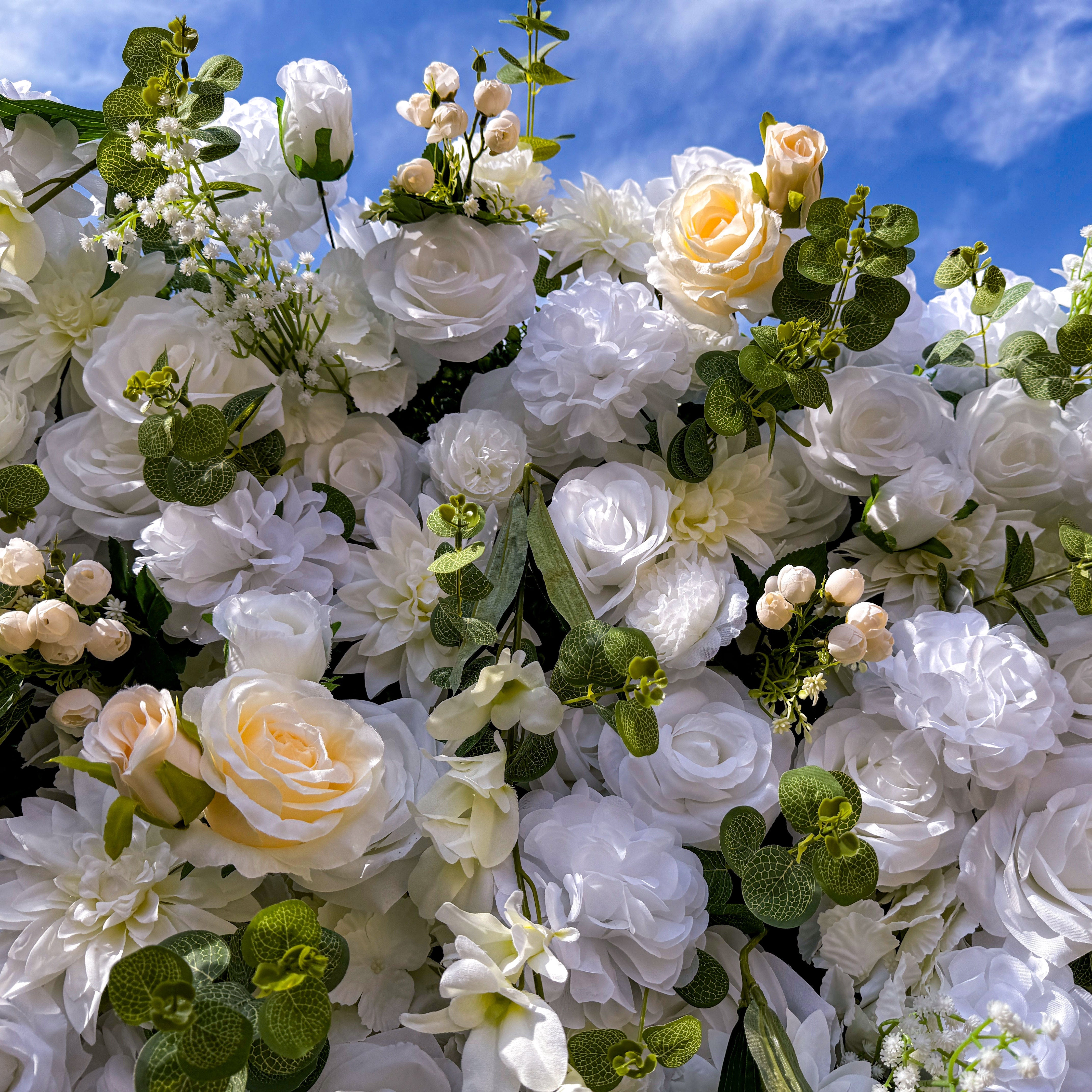 This artificial flower wall is a stunning decoration. It is densely packed with a variety of white and cream - colored flowers, including roses and lilies. The flowers are complemented by lush green leaves, creating a rich and elegant appearance. It is perfect for weddings or events, providing a romantic and beautiful backdrop.