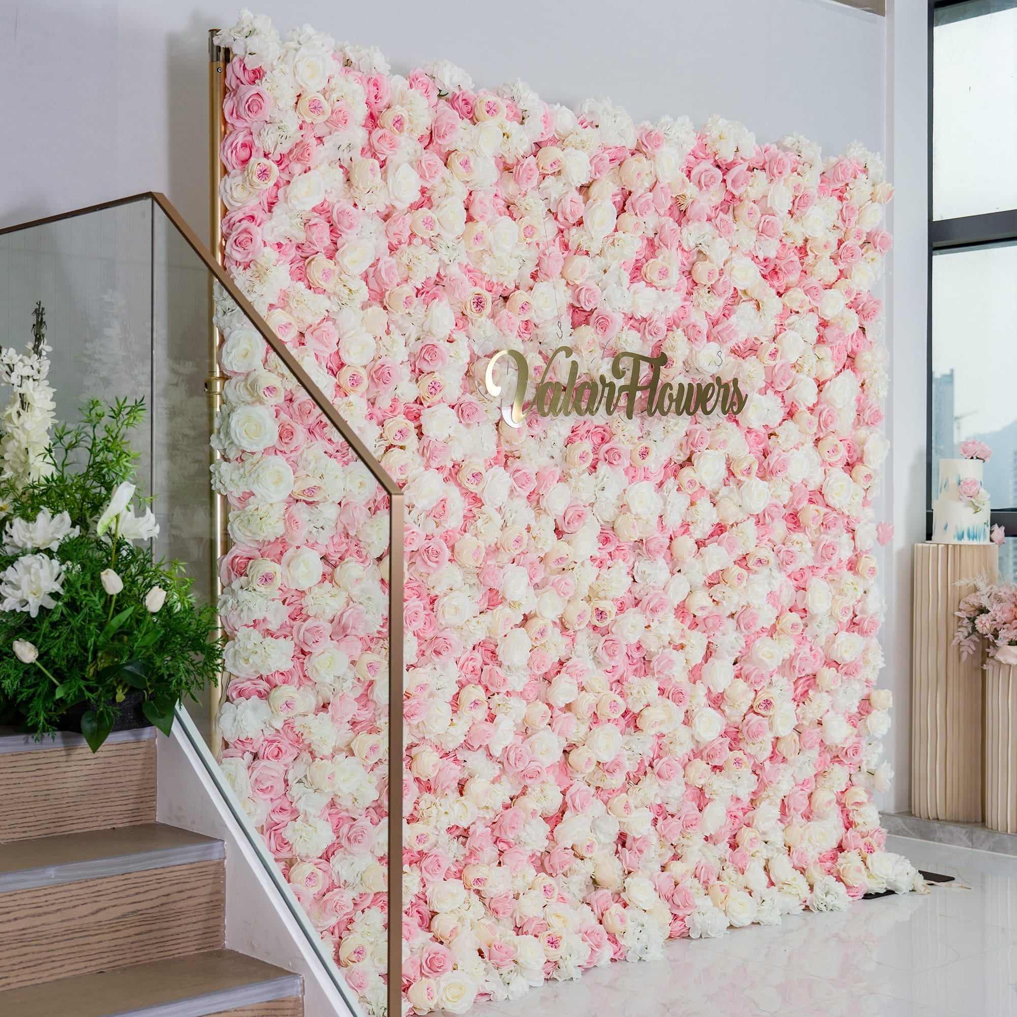 This photo showcases a lush floral backdrop made up of an abundance of pink and white roses. The dense arrangement creates a soft, romantic look with its pastel color palette. The words "Valar Flowers" in elegant gold lettering stand out in the center. Ideal for weddings, bridal showers, or other romantic events, it exudes a dreamy and elegant style. 