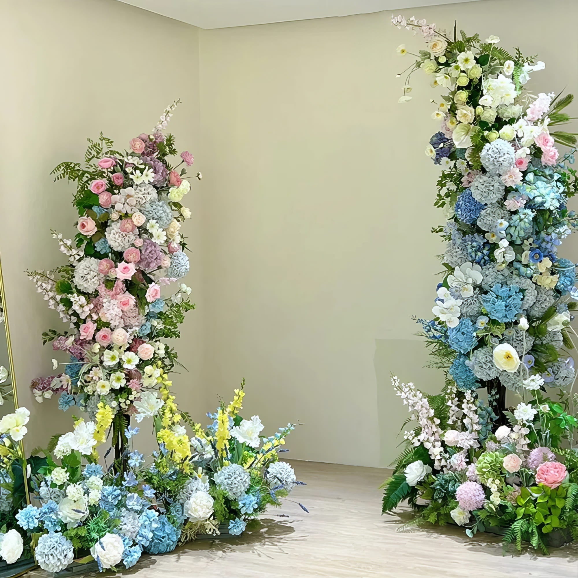 A serene floral display features pastel pink, blue, and white blooms arranged in two vertical columns. The soft colors and lush greenery create a peaceful ambiance, perfect for enhancing any elegant indoor space or event decor.