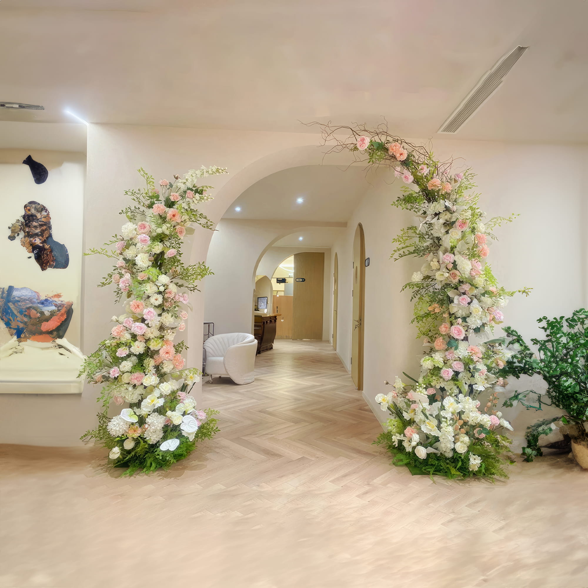 Elegant floral arches with pink and white roses and greenery frame an archway in a sophisticated hallway. The neutral tones and modern decor create a serene and inviting atmosphere, perfect for a chic event or celebration.