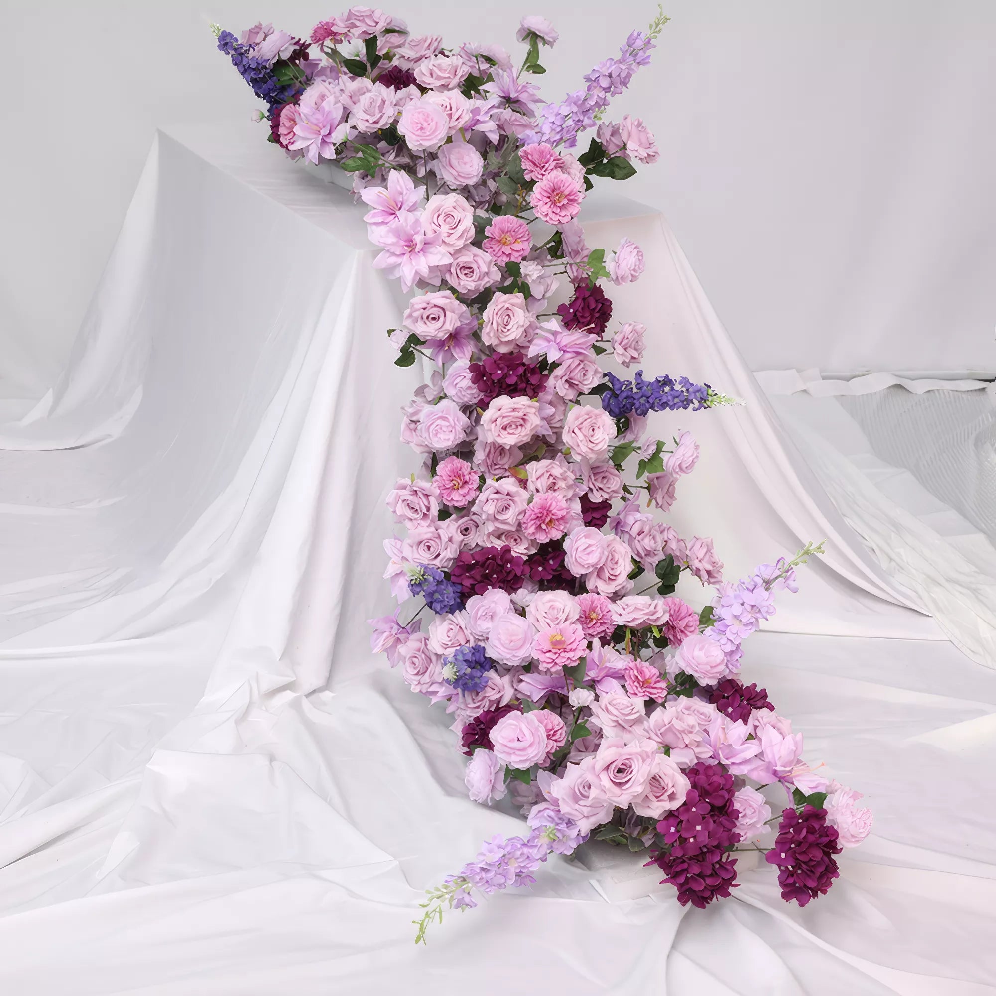 Lavish floral table runner with cascading purple and lavender roses, deep burgundy blooms, and delicate lilac accents. Ideal for creating a luxurious, romantic setting at weddings or special events. The rich hues add elegance and charm to any decor.