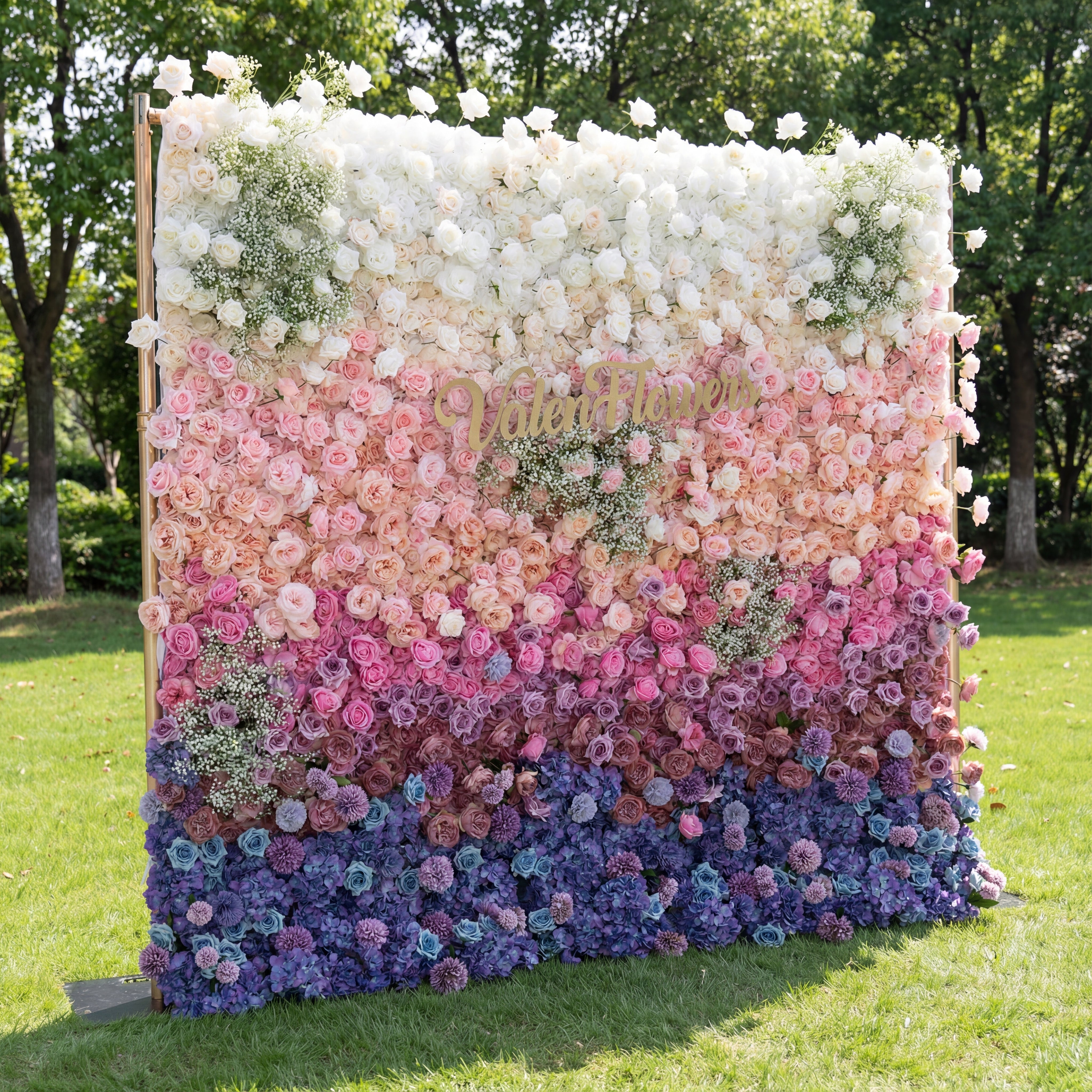 Floral wall with a gradient of white, pink, and purple flowers on a grassy area.